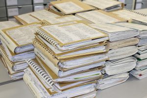 mehr als 10 Stapel von je 5 Spiralbüchern mit maschinegeschriebenen Inhaltsangaben auf dem Buchdeckel liegen auf einem Tisch im Archiv