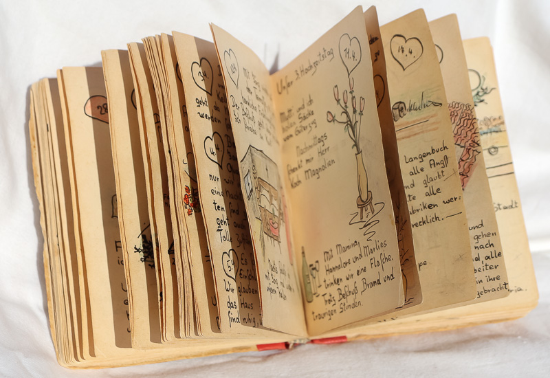 ein aufgeschlagenes Tagebuch vom April mit verschiedenen Zeichnungen und kurzen Sätzen. Zitat: Mit Mamma, Hannelore und Marlies trinken wir eine Flasche. Tritz Beschuß, Brand und traurigen Stunden.