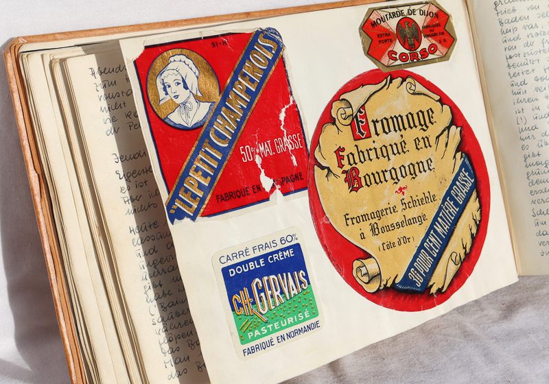die Seite des aufgeschlagenen Tagebuchs zeigt vier bunte Aufkleber von Käse und Senfpackungen