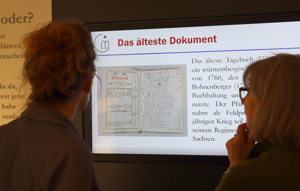 zwei Besucherinnen vor einer Medienwand die das älteste Dokument des Archivs erläutert