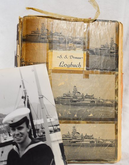 vor dem mit vielen Klebestreifen zusammengehaltenen Logbuch das Foto eines lachenden jungen Mannes in Uniform