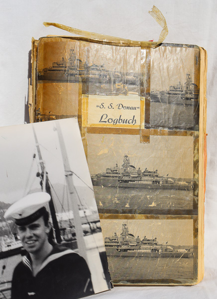 vor dem mit vielen Klebestreifen zusammengehaltenen Logbuch das Foto eines lachenden jungen Mannes in Uniform
